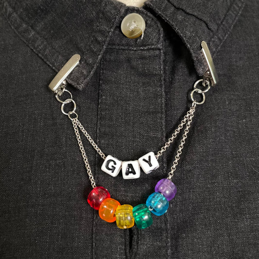 Silver Tone two-tiered chain connected by clips to a shirt collar. The first tier of chain has plastic letter beads spelling "GAY" and the second tier has 6 pony beads in rainbow color order. 